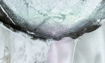 Gloved hand working woven fibreglass cloth over a curved mould, with frayed cloth edges hanging below