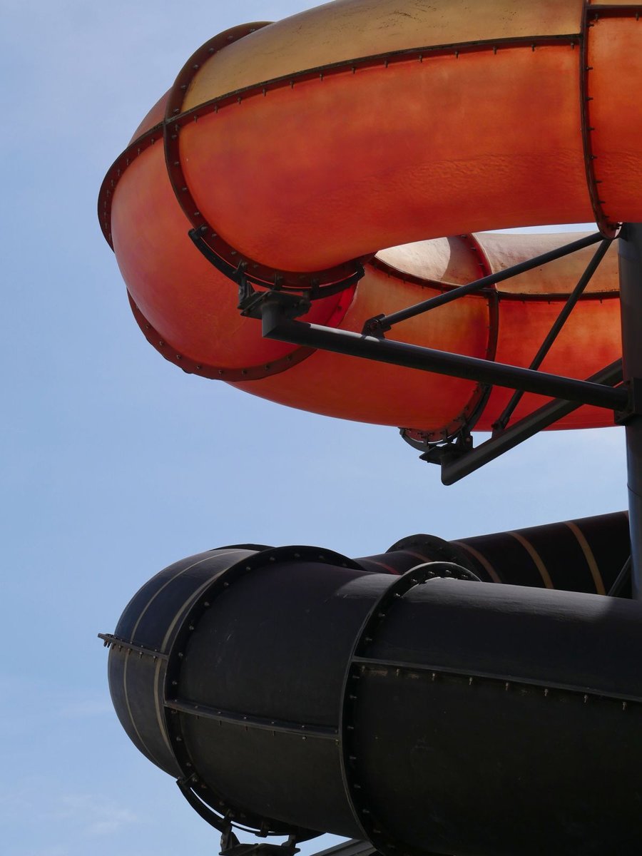 A curving orange and black water slide tube against a blue sky
